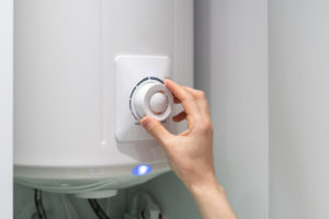 Hand adjusting temperature on bathroom electric boiler hanging on wall, using control knob.