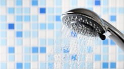 Shower head with water running and blue and white tiles behind